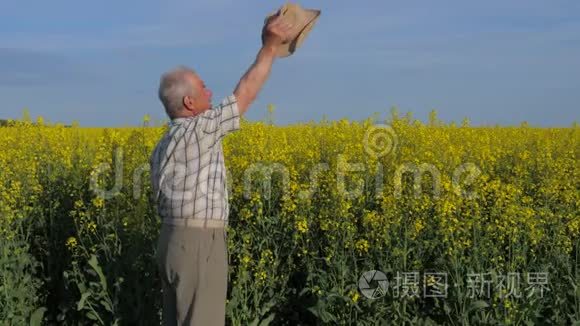 年长的白发农夫在一片田野里，挥舞着他的手臂和帽子打招呼。