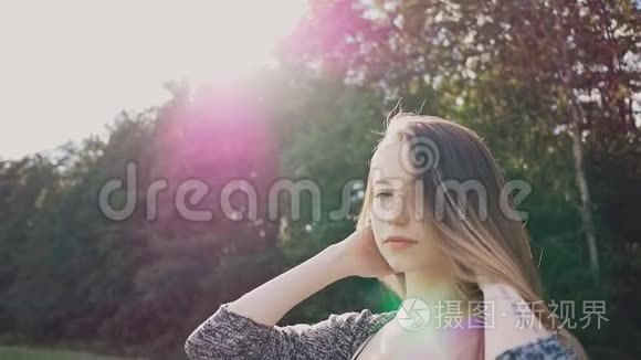 年轻而迷人的女孩在美丽的紫色晚霞中的绿树背景上对着镜头摆姿势