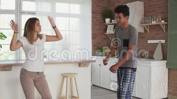 早上在家快乐的年轻夫妇穿着睡衣在厨房里跳舞听音乐。 一对夫妇