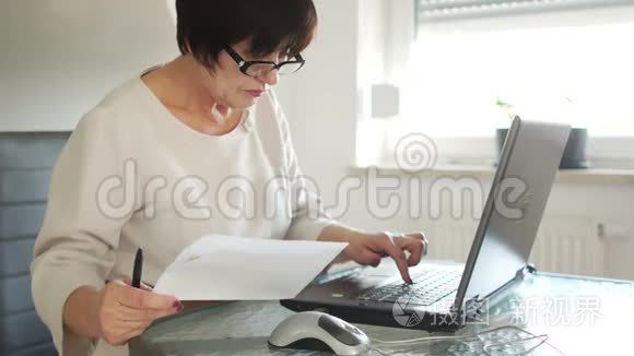 商业女性使用电脑、互联网支付、网上银行支付账单。 她手里拿着笔和纸