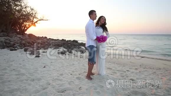 新娘和新郎在黎明时拥抱沙滩并开怀大笑