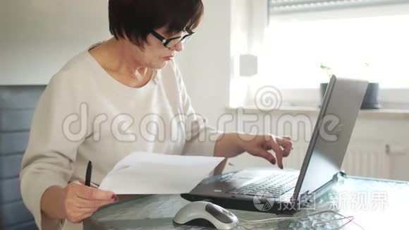 一个穿着商务服和眼镜的女人正在用她的笔记本电脑工作。 附近有纸账.. 愿意考虑