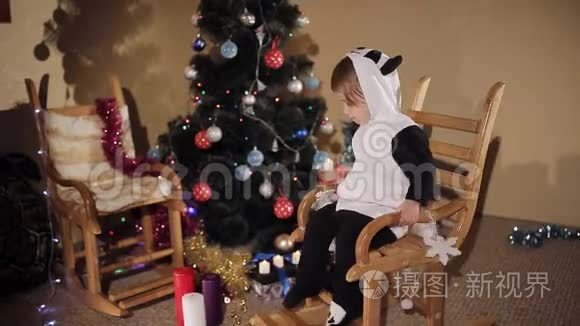 在圣诞树和蜡烛的背景下，孩子在摇椅上摇摆。 圣诞节的气氛。