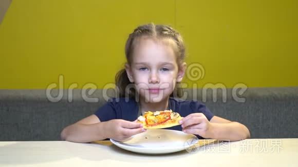 小女孩在有黄色墙壁的咖啡馆里吃披萨的肖像。 在慢动作中