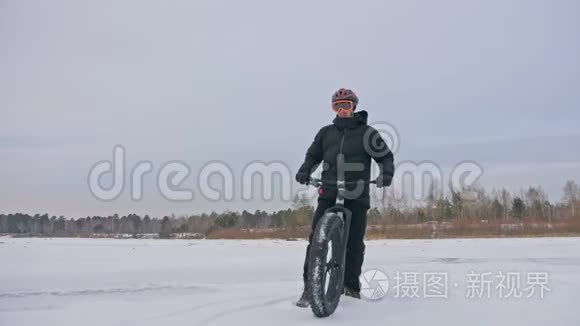 专业的极限运动员自行车站在户外一辆胖自行车。 骑自行车者在冬天的雪林中退缩。 男人走路