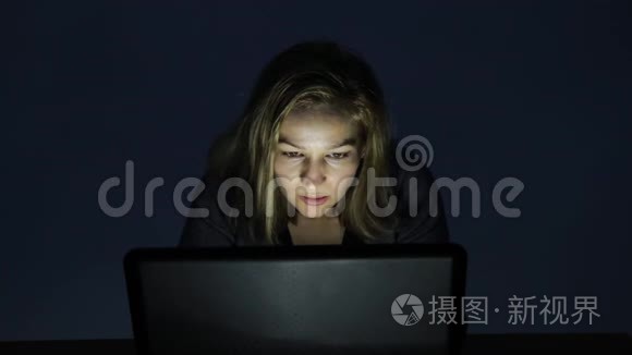 戴眼镜的女人在黑暗的房间里用电脑，看着显示器，开始高兴起来