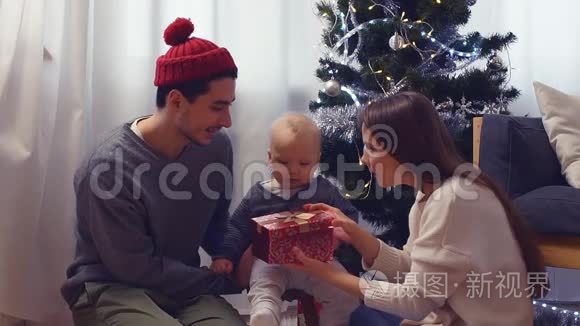 家中圣诞树附近有圣诞礼物的家庭和宝宝。 儿童打开礼品盒。