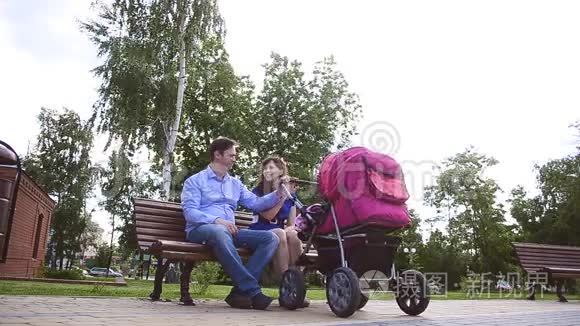 爸爸妈妈和婴儿车在公园的长凳上休息。