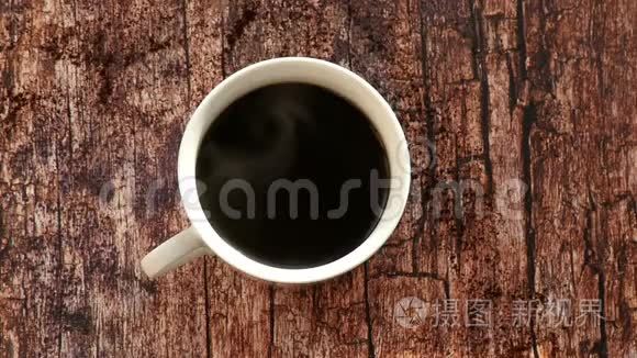 在白色的杯子上端着咖啡。 木桌上一杯咖啡，俯视图.. 慢动作
