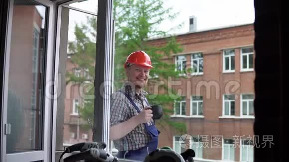 一个工人喝一杯黑杯子里的热饮料，对着一座砖楼。