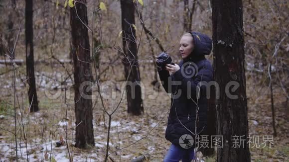 女孩摄影师走在秋天的森林里，拍摄大自然的照片。 电影镜头，慢动作。 第一场雪