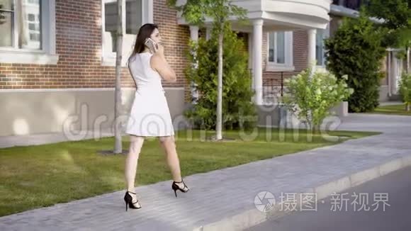 一个年轻的女人走在街上，经过精英住宅，这位女士正在用手机通话，看起来很忙