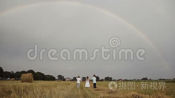一个女孩和两个男孩用稻草棒跑着一片黄色的田野，迎接彩虹