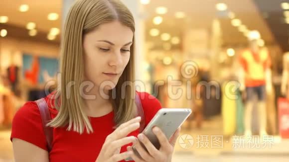 年轻漂亮的女人坐在购物中心微笑。 用她的智能手机和朋友聊天