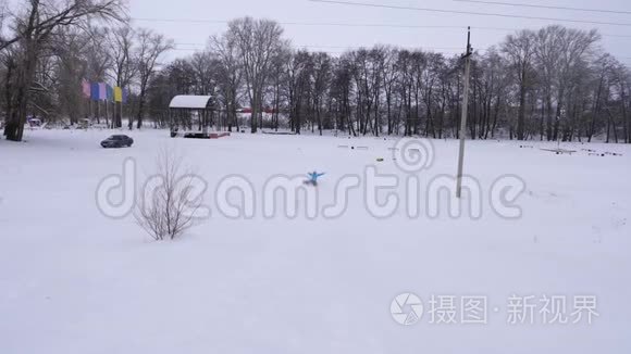 快乐的年轻女孩滑下雪滑到充气雪管上，挥动她的手。 女孩在公园里玩