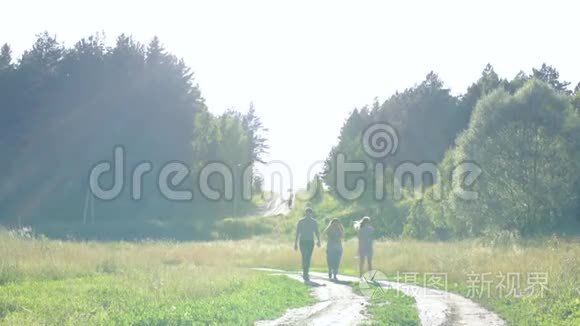 两个女孩和一个男人在夏天的时候，在日落的好天气里沿着乡间小路和森林散步