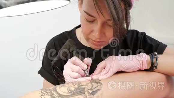 纹身大师迷人的女人与可怕的纹身客户的女孩在臀部。 黑色纹身机和墨水