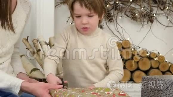 一个严肃的小男孩帮他妈妈剪圣诞礼物的包装纸