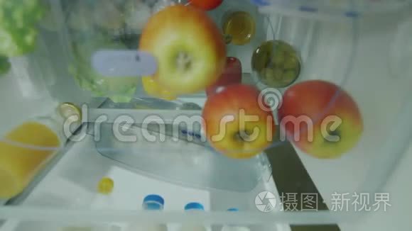 简单的水果小吃。 一个饥饿的女人打开冰箱，拿一个苹果吃。 从冰箱内观看