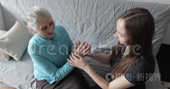 一个漂亮的年轻女孩正在家里抚摸她祖母那双老皱的手。