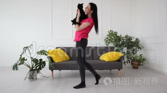 对宠物的爱。 漂亮的黑发女孩和一只黑猫在客厅的家里跳舞