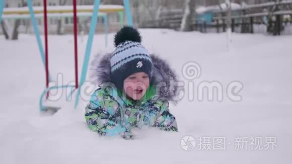 一个小孩在冬天的公园里玩雪.. 躺在白色蓬松的雪上微笑的婴儿。 新鲜的乐趣和游戏