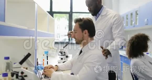 在现代实验室工作的不同的科学家小组，两位男性同事讨论试管中的例子
