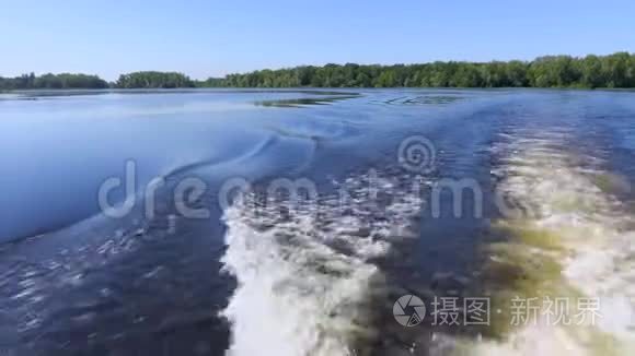 船尾的录像。 浪，在水面上醒来.. 夏天的河流或湖泊。 蓝天