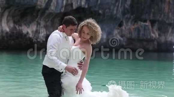 新娘和新郎站在海滩的浅水处，在水面上穿上衣服