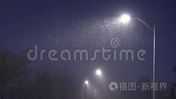 雪落在灯柱的背景下。 夜冬路灯伴落雪..