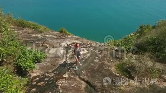 空中年轻快乐的徒步旅行者女孩站在山岩上，张开双臂，微笑。 泰国Koh Phangan。