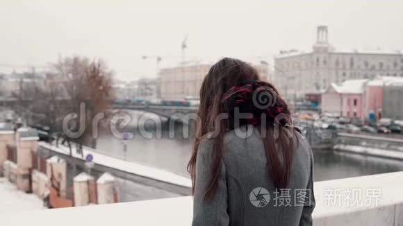 后景。 站在桥上悲伤的黑发女孩叹了口气，看着白雪覆盖的冬季小镇。