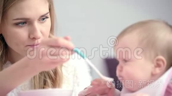 年轻的母亲喂养婴儿。 年轻妈妈用勺子喂孩子