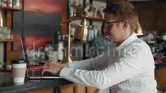 年轻的男性自由职业者在自然美食咖啡馆里坐在打开的笔记本电脑前，一边用手机聊天