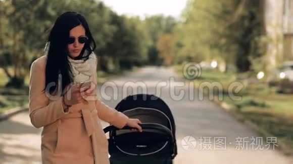 一个年轻的女孩带着婴儿车穿过公园，在电话里交谈