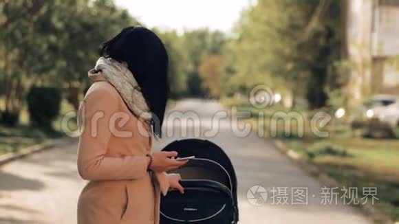 一个年轻的女孩带着婴儿车穿过公园，在电话里交谈