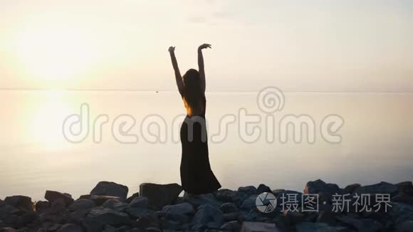 穿着黑色长裙在日落时分在沙滩上跳舞的无忧无虑的女人