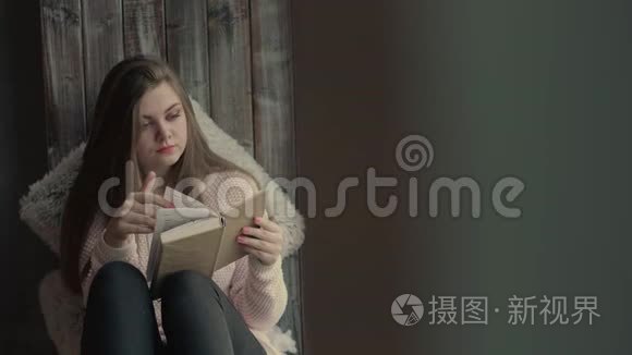 一位美丽的年轻女子坐在窗户上，看着一本书翻页
