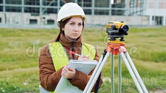 穿绿色工作服和头盔的年轻女性测量员调整设备，计算并写信给