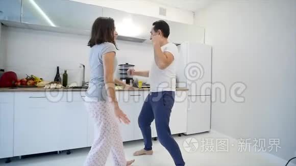 早上在家幸福的年轻夫妇穿着睡衣在厨房里听音乐跳舞。 慢动作