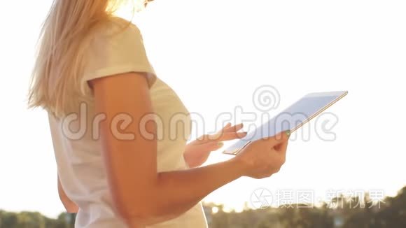 女性手在平板电脑上打字，背景是海上日落。 慢动作