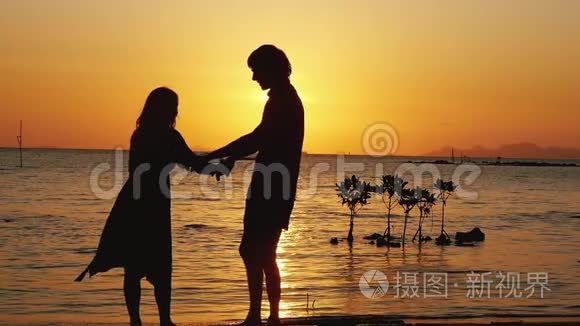 迷人的男人和女人在日落时在海边旋转。 恋爱中的情侣在度假时一起玩