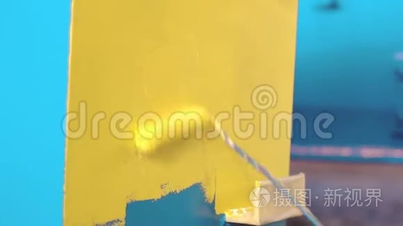 人正在用手辊把蓝色的金属细节画成黄色。 工厂的油漆工