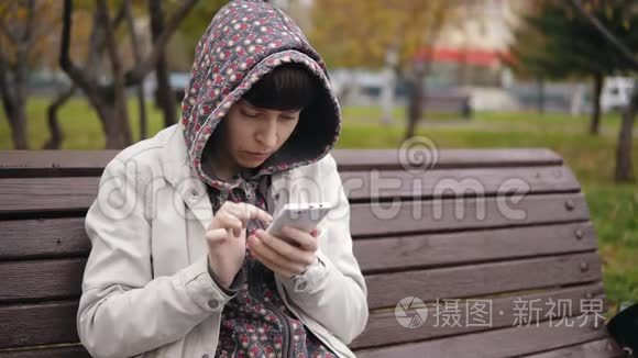 一位身穿连帽衫的年轻女子在秋季公园使用智能手机。