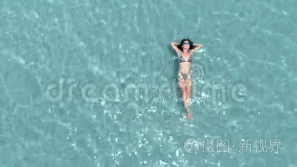 美丽的年轻女子漂浮在晶莹剔透的水中，空中旋转拍摄