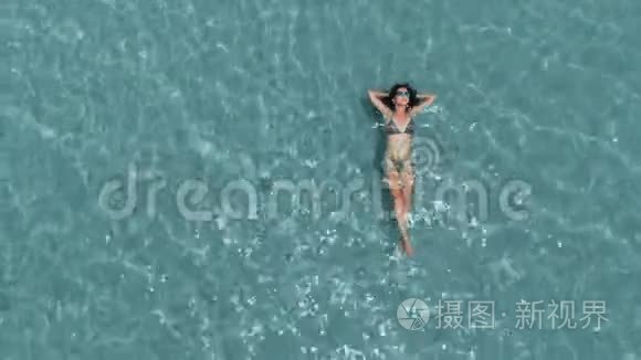 美丽的年轻女子漂浮在晶莹剔透的水中，空中旋转拍摄