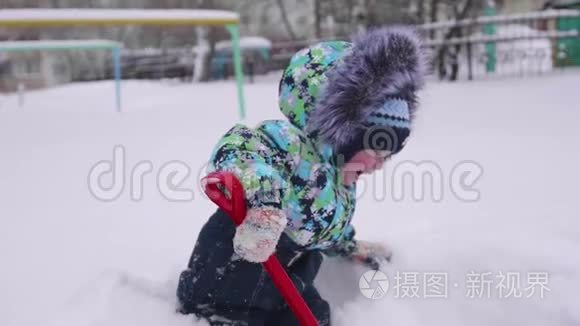 一个小孩在冬天的公园里玩雪.. 孩子拿着铲子，公园里有很多雪。 有趣的游戏