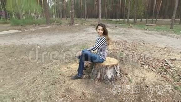 一位美丽的年轻女子坐在夏天的松树公园的树桩上