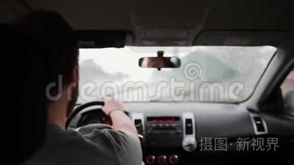 雨中驾驶汽车的人的后景.. 手放在方向盘上，雨刷在工作。