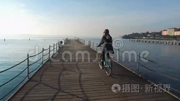 4K. 在阳光明媚的日子里，快乐的女孩骑着自行车在码头上的蓝海上空。 休假时间